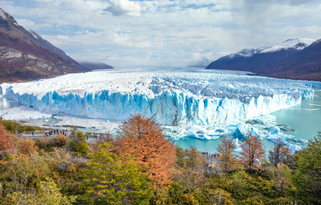 Vue spectaculaire du glacier Perito Moreno en Patagonie, avec ses immenses parois de glace bleutées contrastant avec les forêts colorées et les montagnes environnantes, destination emblématique des voyages d’aventure Karavaniers.