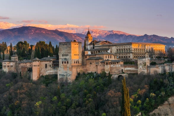 Vue sur l’Alhambra de Grenade au coucher du soleil, avec la Sierra Nevada en arrière-plan.