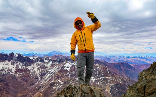 Personne en veste jaune au sommet d'une montagne enneigée.