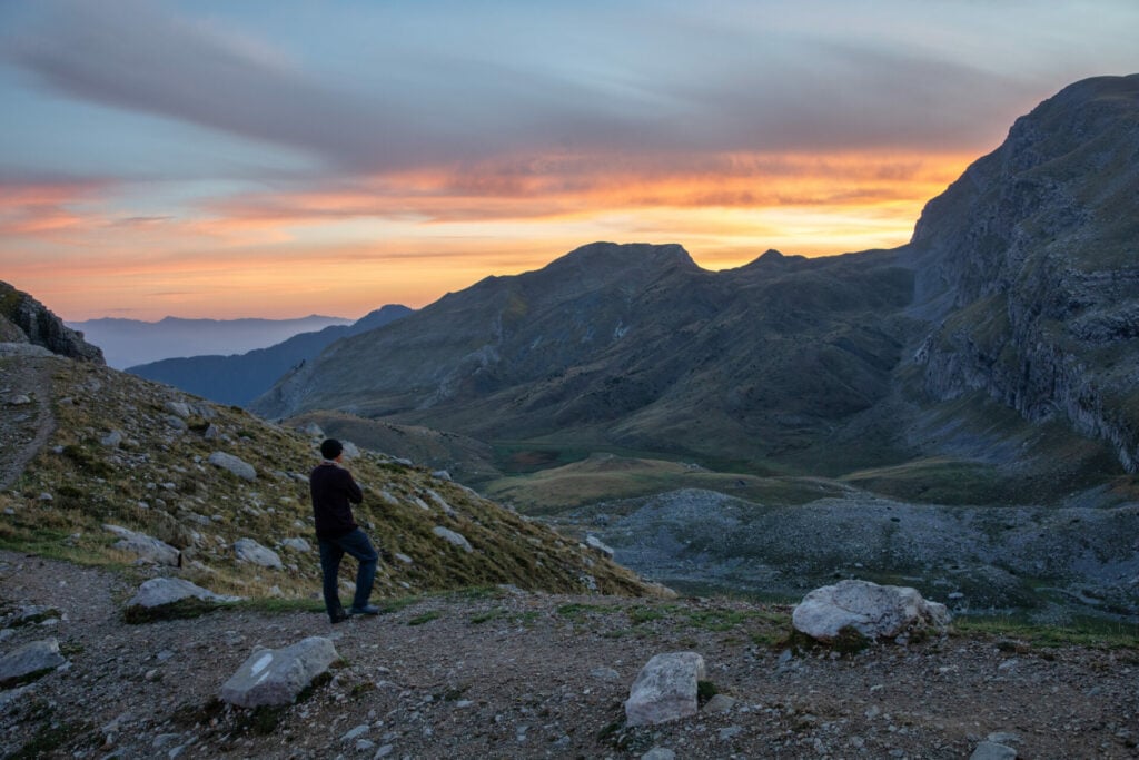 Personne contemplant un coucher de soleil sur les montagnes des Balkans, entre ombres douces et lumière dorée.