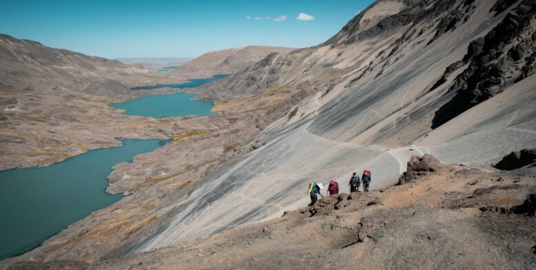 Groupe progressant en file sur une crête aride dominant un lac glaciaire turquoise