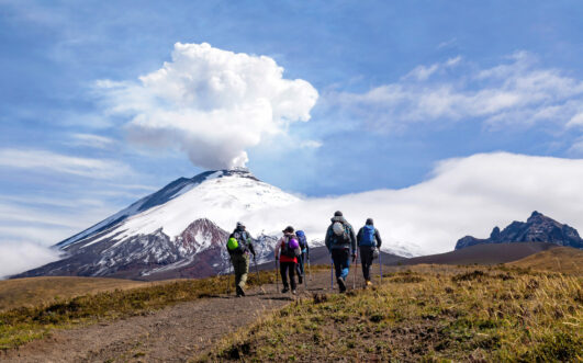 Randonneurs équipés de sacs à dos et bâtons marchant vers le volcan Cotopaxi fumant en Équateur.