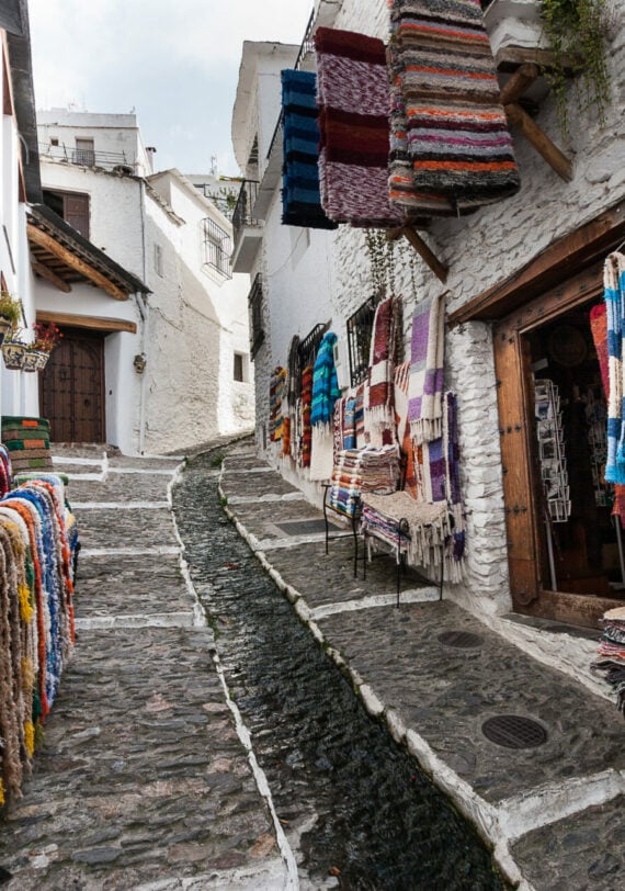 Ruelle pavée d’un village andalou avec des tapis colorés accrochés. Demander à ChatGPT