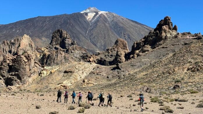 Groupe de randonneurs marchant dans un paysage volcanique avec un sommet en arrière-plan