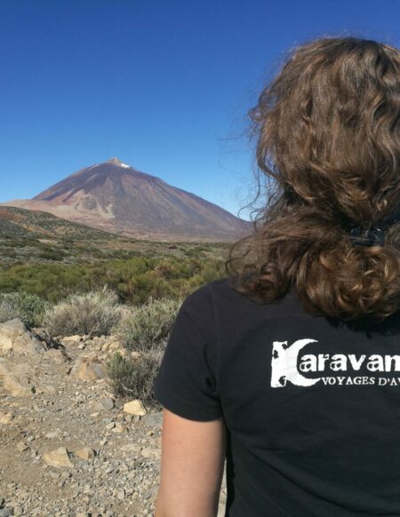 Julie Betelu, guide Karavaniers de dos, portant un t-shirt avec le logo Karavaniers et observant un volcan au loin sur les îles Canaries