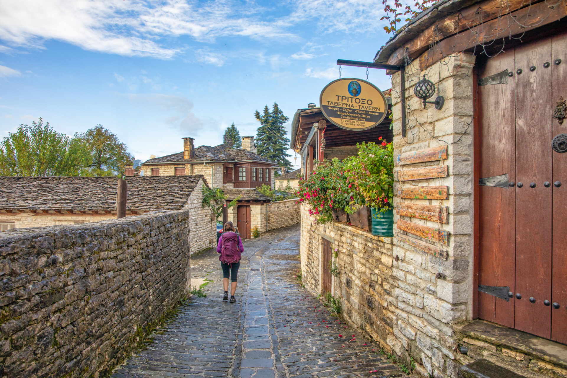 Scène de village dans le Zagori : ruelles pavées, maisons en pierre et une marcheuse au lever du jour.