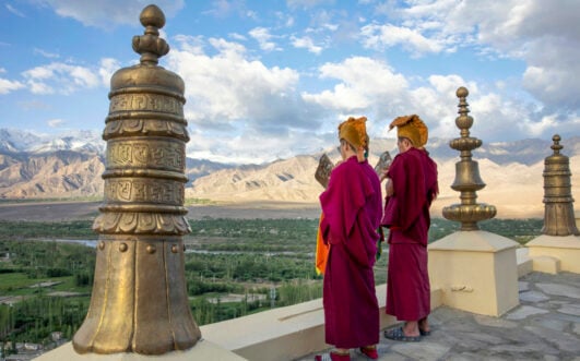 Deux moines bouddhistes en robes rouges contemplant les montagnes arides du Ladakh. Trek en Asie himalayenne avec Karavaniers.