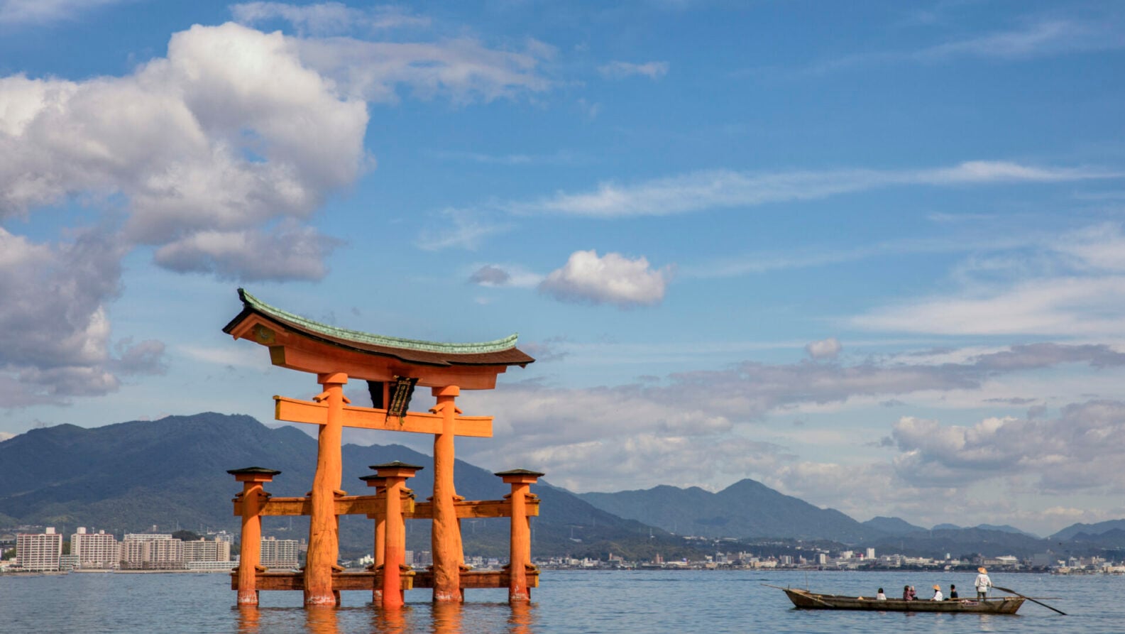 Torii vermillon de Miyajima flottant sur l’eau, avec les montagnes en toile de fond.