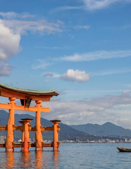 Torii vermillon de Miyajima flottant sur l’eau, avec les montagnes en toile de fond.