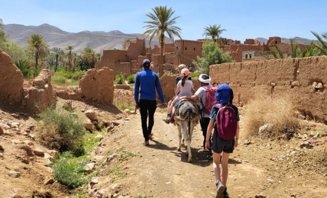 Marcheurs accompagnés d’un muletier traversant un village en terre aux portes du Sahara