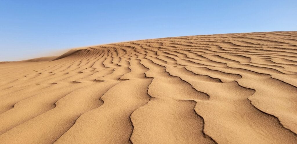 Une dune de sable avec des vagues vous invite à une aventure à travers le désert, où les sables dorés ondulent sous le soleil. - Karavaniers