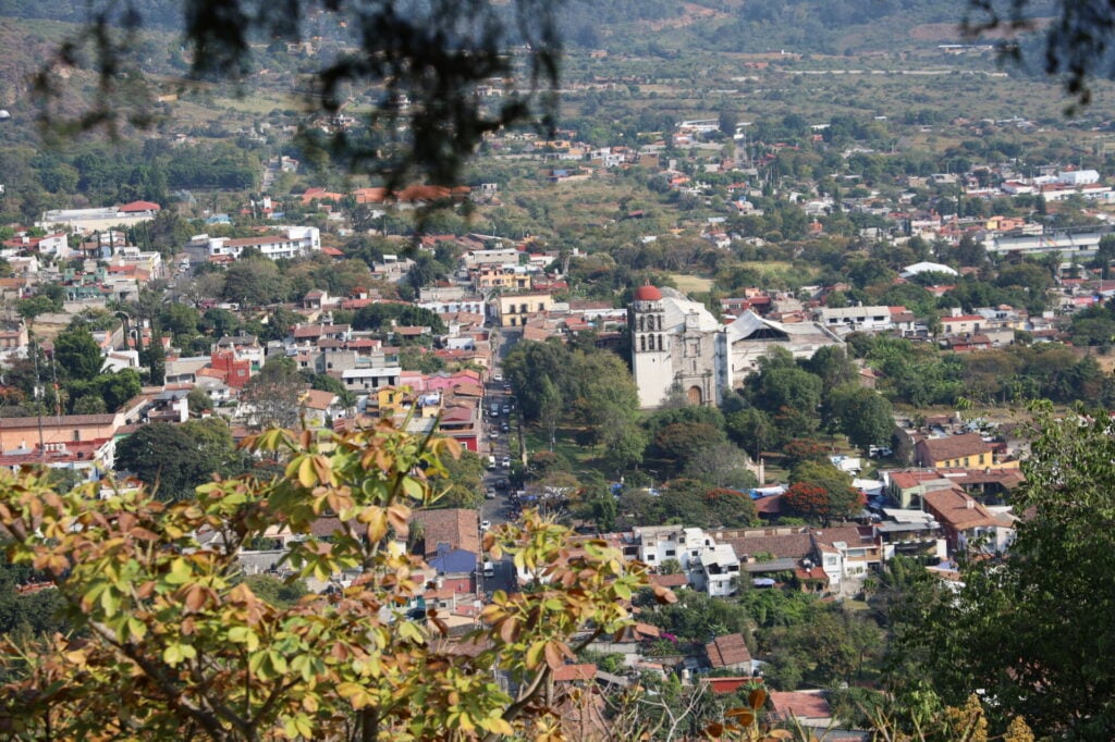 Vue d'une petite ville, désignée comme l'un des Pueblos Mágicos, avec une église historique proéminente au centre, entourée d'arbres, de bâtiments résidentiels et de verdure, vue d'un point d'observation élevé près des Volcans du Mexique. - Karavaniers