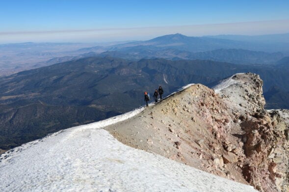Randonneurs progressant sur une crête enneigée au sommet d’un volcan mexicain.