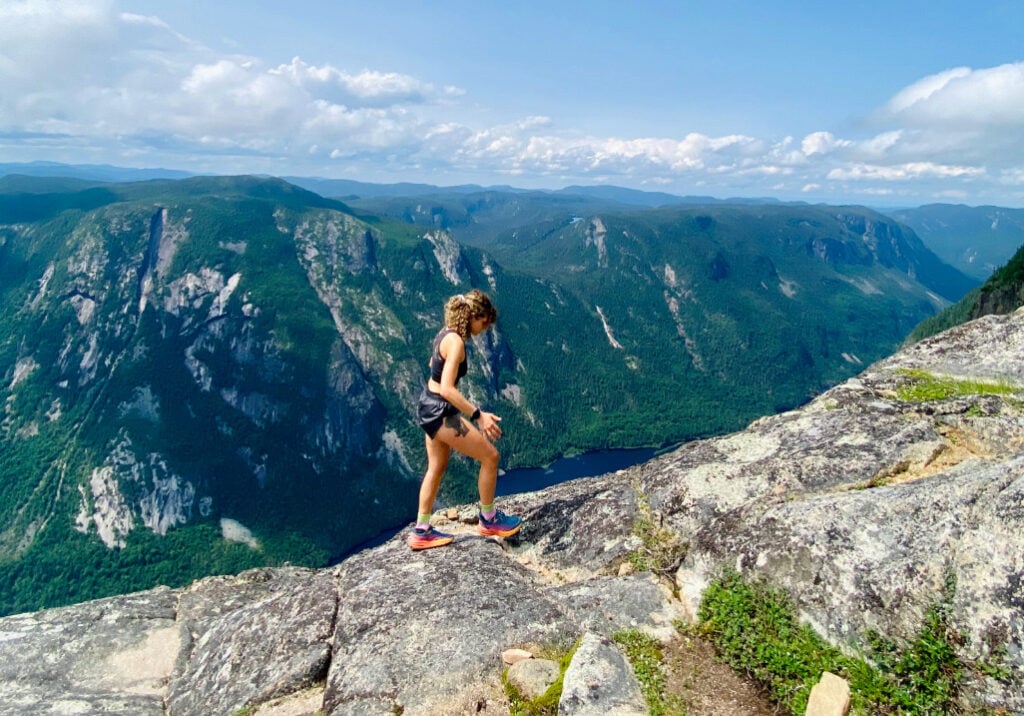Océane Martinez en randonnée sur un plateau rocheux, surplombant un immense canyon verdoyant sous un ciel bleu éclatant.