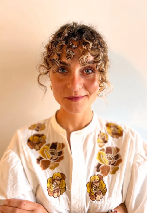 Portrait de Océane Martinez portant une chemise fleurie devant un mur blanc.