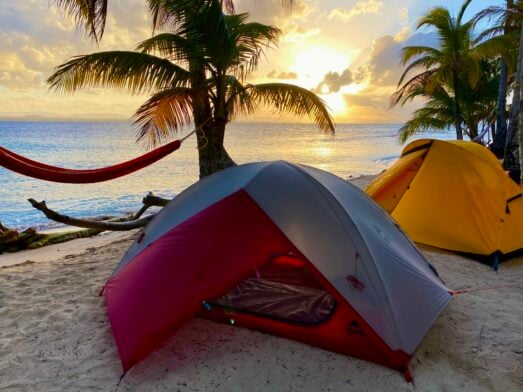 Tente de bivouac installée entre cocotiers, face à la mer
