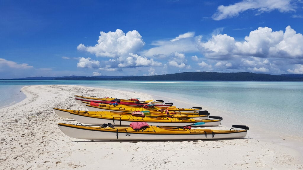 Kayaks alignés sur une plage de sable blanc sous un ciel tropical
