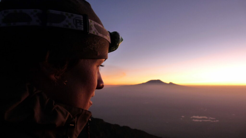 Randonneuse/alpiniste au lever du soleil depuis le sommet du mont Méru en Tanzanie. Elle regarde, au loin, le Kilimandjaro lors de son voyage d'expédition avec un groupe Karavaniers.