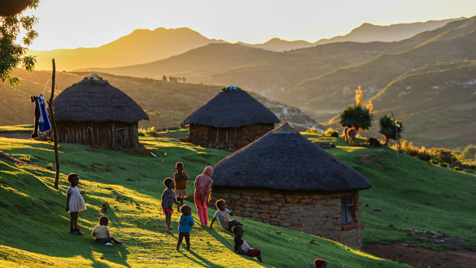 Village traditionnel du Lesotho au lever du soleil, huttes rondes en pierre et habitants en habits colorés