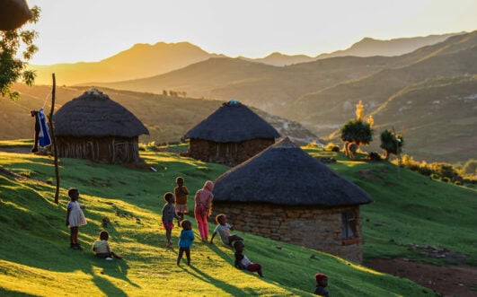 Village traditionnel du Lesotho au lever du soleil, huttes rondes en pierre et habitants en habits colorés