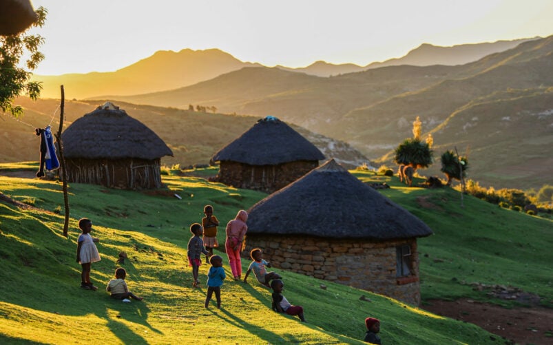 Village traditionnel du Lesotho au lever du soleil, huttes rondes en pierre et habitants en habits colorés