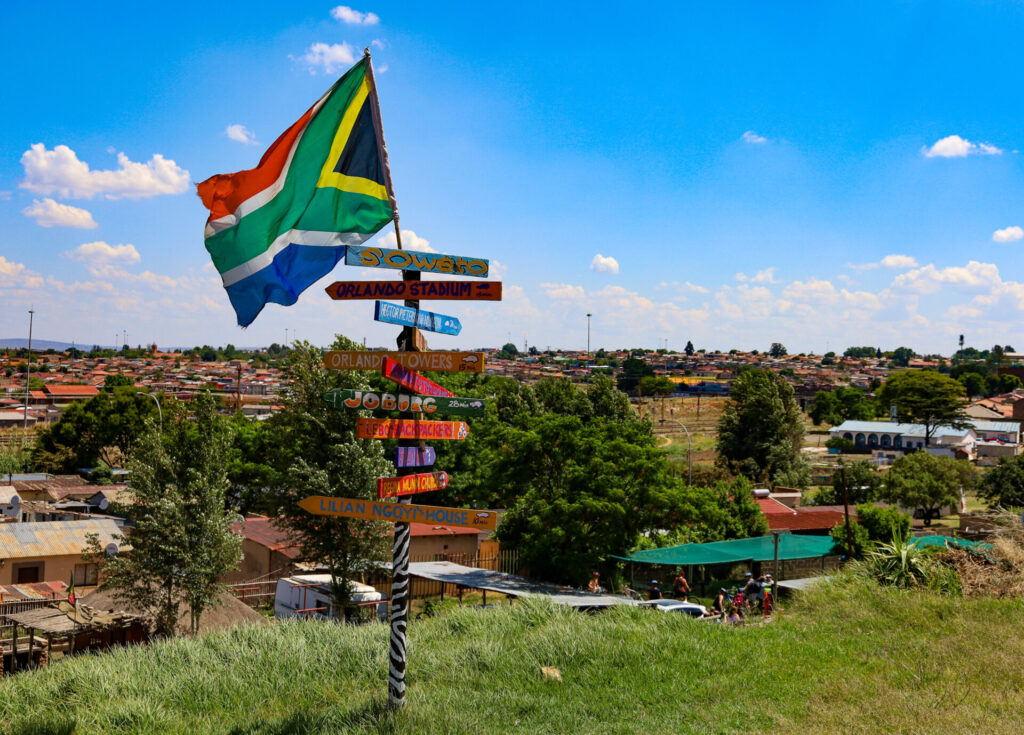 Drapeau sud-africain et panneau directionnel, scène colorée de village.