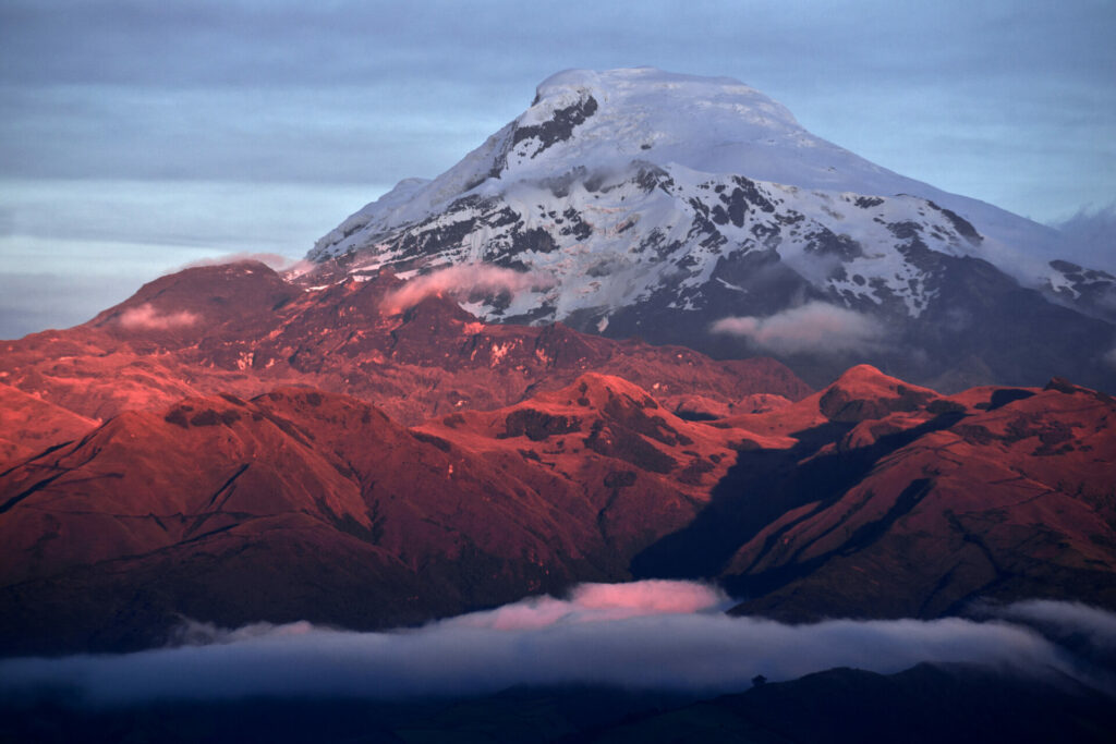 Sommet enneigé du volcan Chimborazo en Équateur, baigné par les teintes rosées du lever ou coucher de soleil, dominant les montagnes andines.