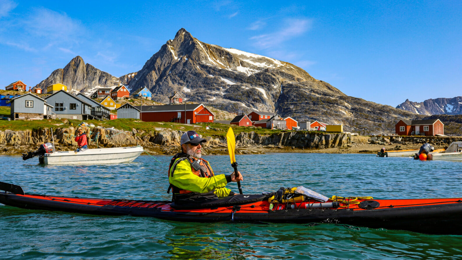 Kayakiste en tenue sèche naviguant dans un fjord, maisons rouges sur la côte