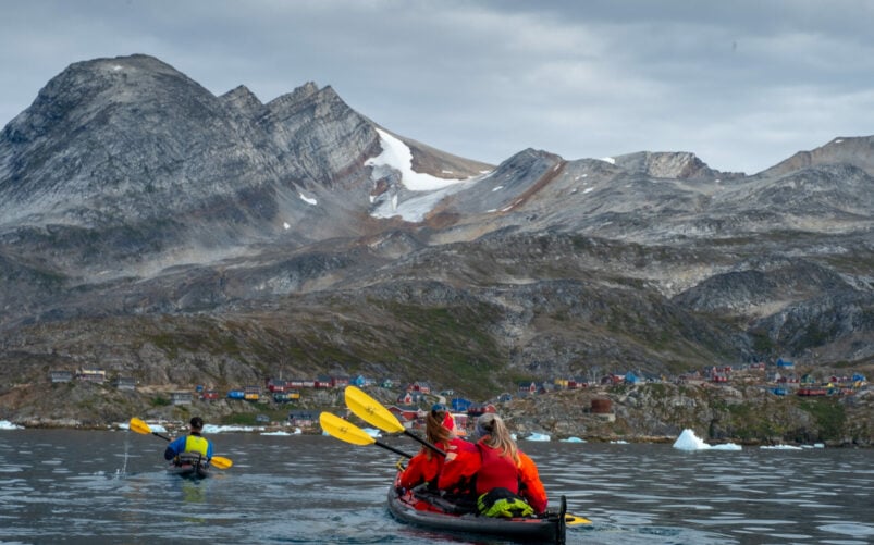 Kayakistes pagayant devant des montagnes rocheuses au Groenland.