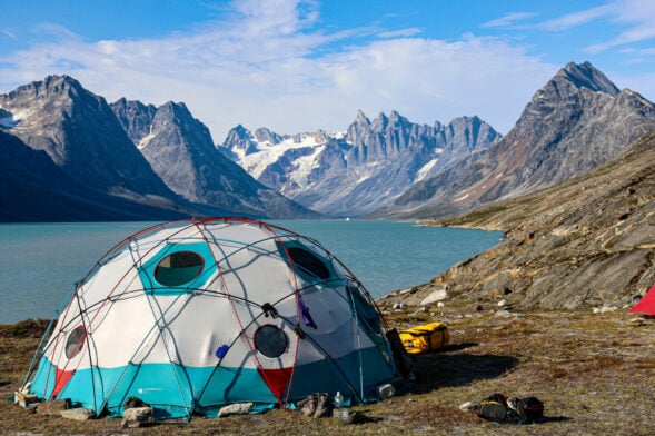 Campement de dômes au bord d’un fjord turquoise, glaciers en arrière-plan