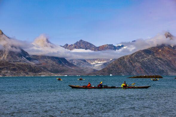 Kayakistes glissant sur une mer calme, avec glaciers et sommets en toile de fond.