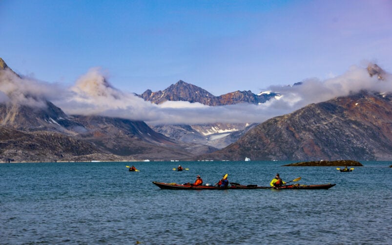 Kayakistes glissant sur une mer calme, avec glaciers et sommets en toile de fond.