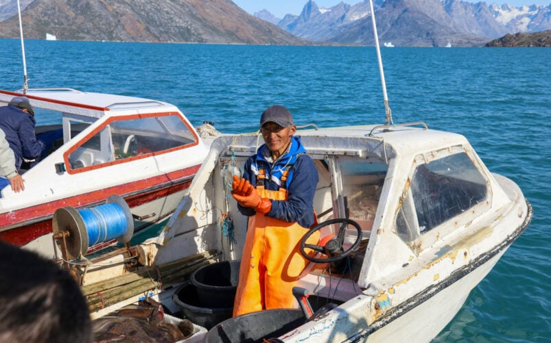 Pêcheur groenlandais assis à bord de son bateau, outils à la main et mer calme