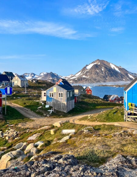 Maisons colorées au bord d’un fjord au Groenland, avec montagnes enneigées en arrière-plan.