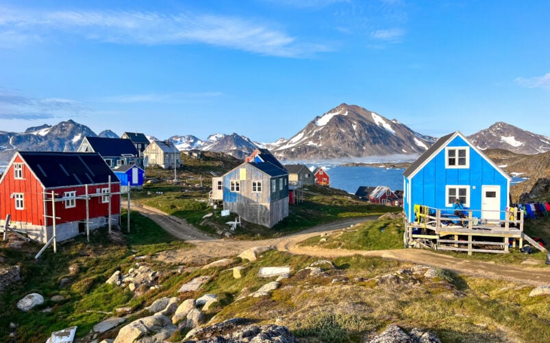 Maisons colorées au bord d’un fjord au Groenland, avec montagnes enneigées en arrière-plan.