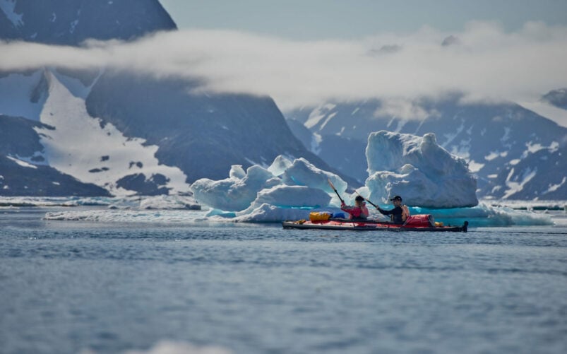 Groupe de kayaks rouges naviguant entre les icebergs et les pics enneigés du Groenland