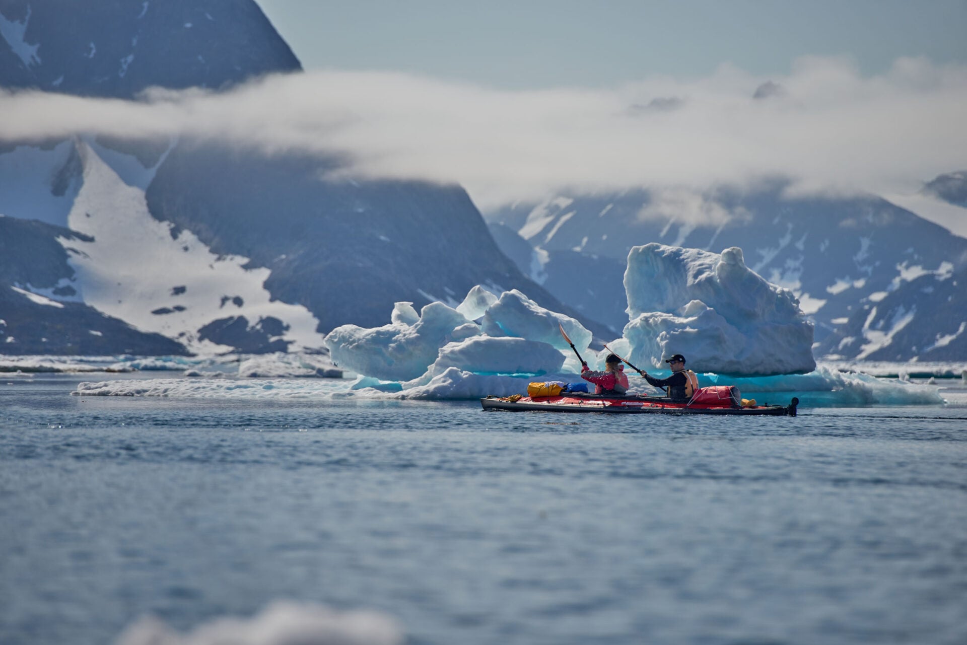 Groupe de kayaks rouges naviguant entre les icebergs et les pics enneigés du Groenland