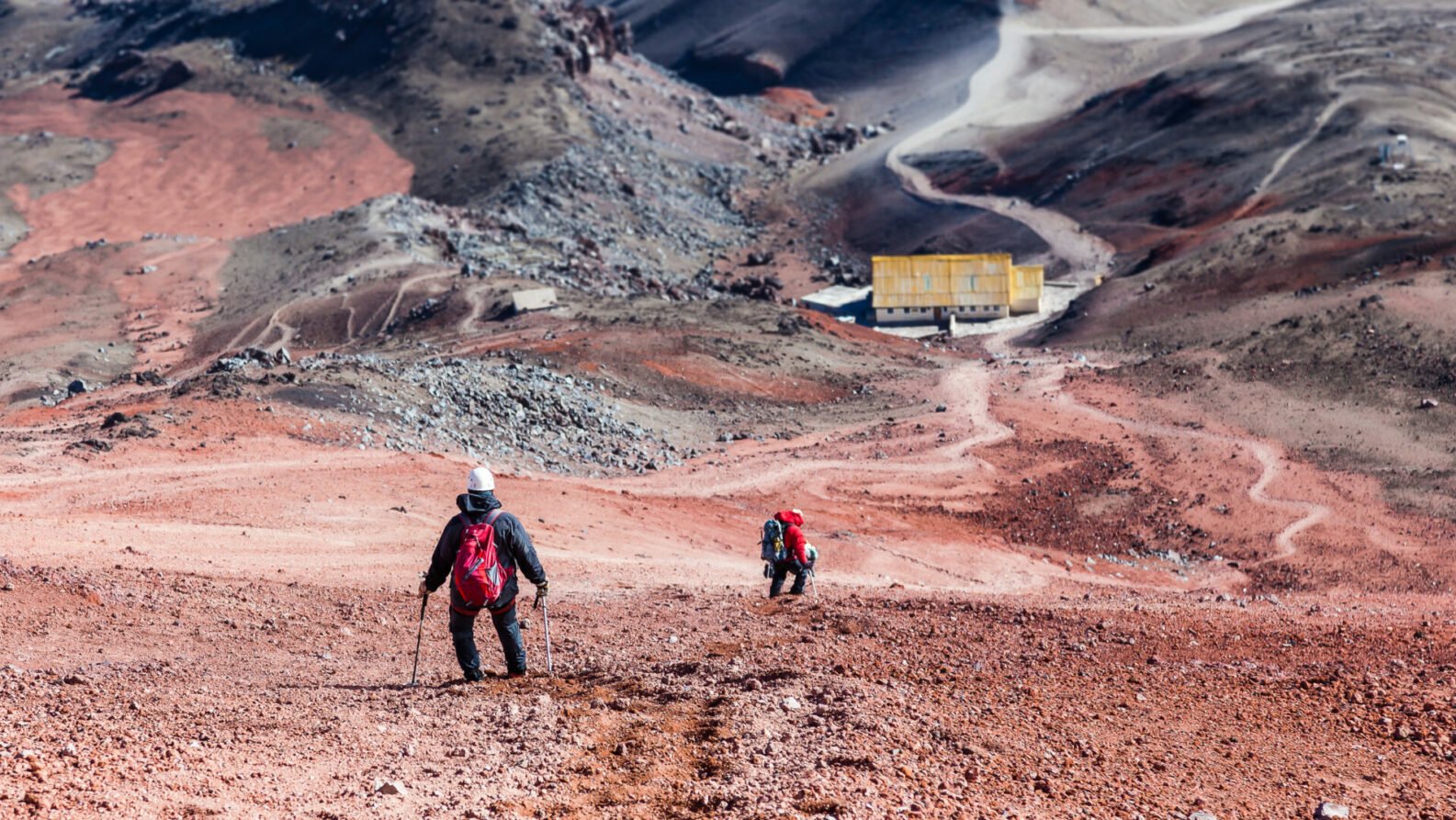 Randonneurs montant une pente volcanique rouge vers un refuge.