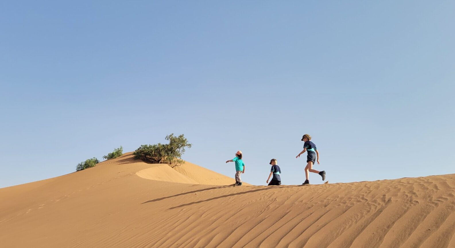 Marche familiale sur une dune dorée, sous un ciel dégagé dans le désert marocain