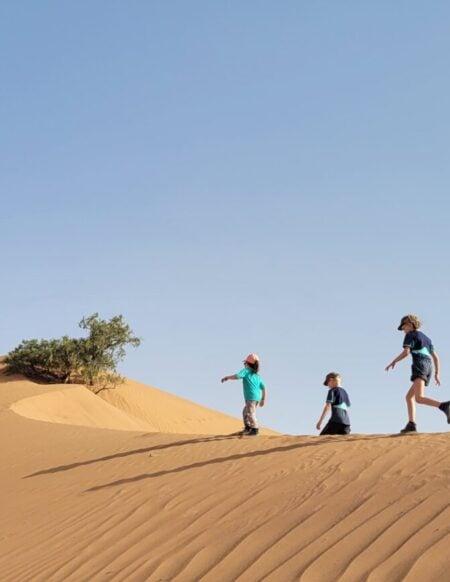 Marche familiale sur une dune dorée, sous un ciel dégagé dans le désert marocain