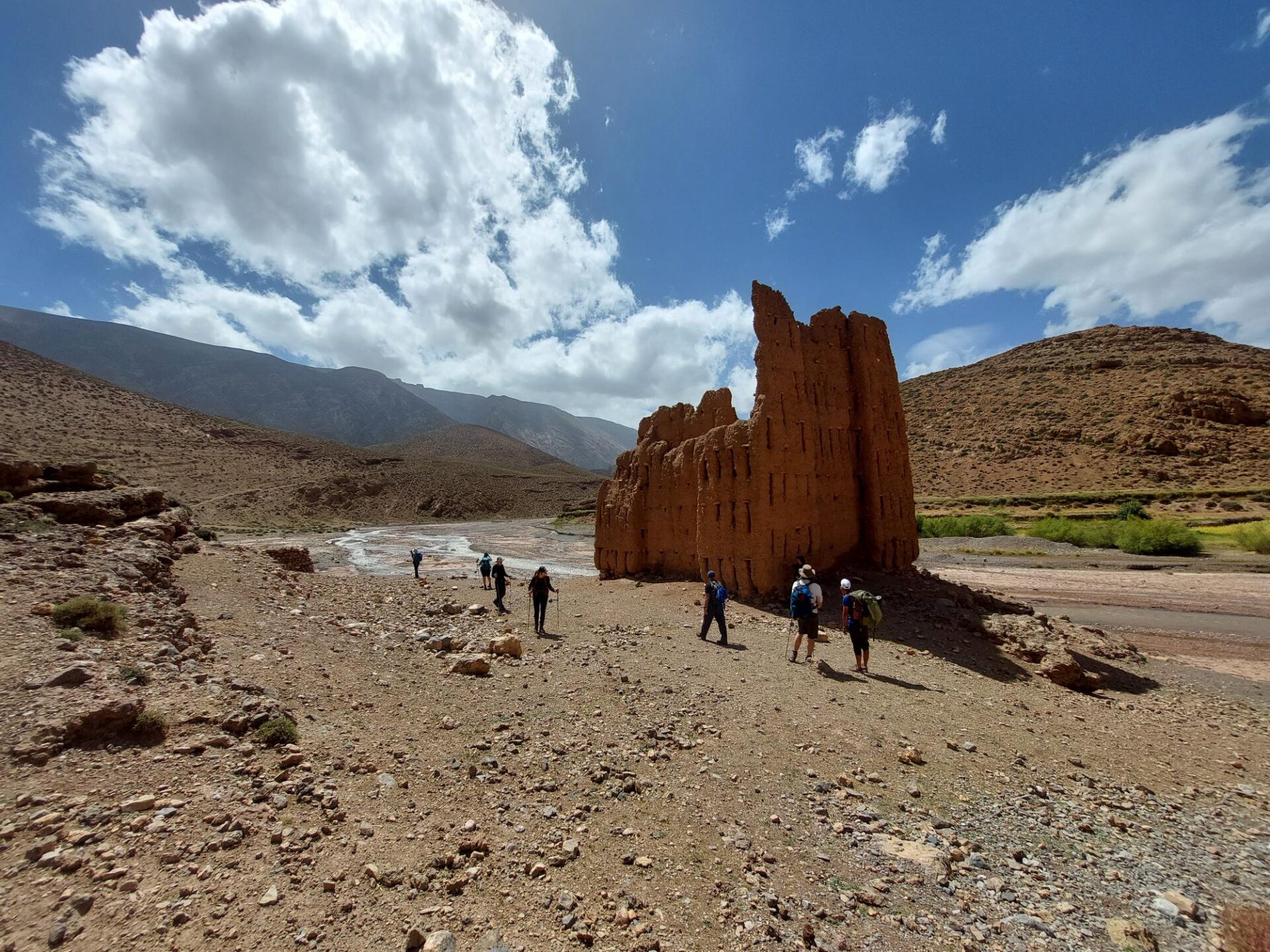 Randonneurs marchant près d’une ruine en pisé dans un paysage semi-désertique du Maroc