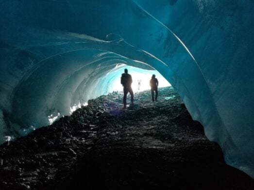 Explorateurs marchant à l’intérieur d’un tunnel de glace bleu turquoise sous un glacier bolivien.