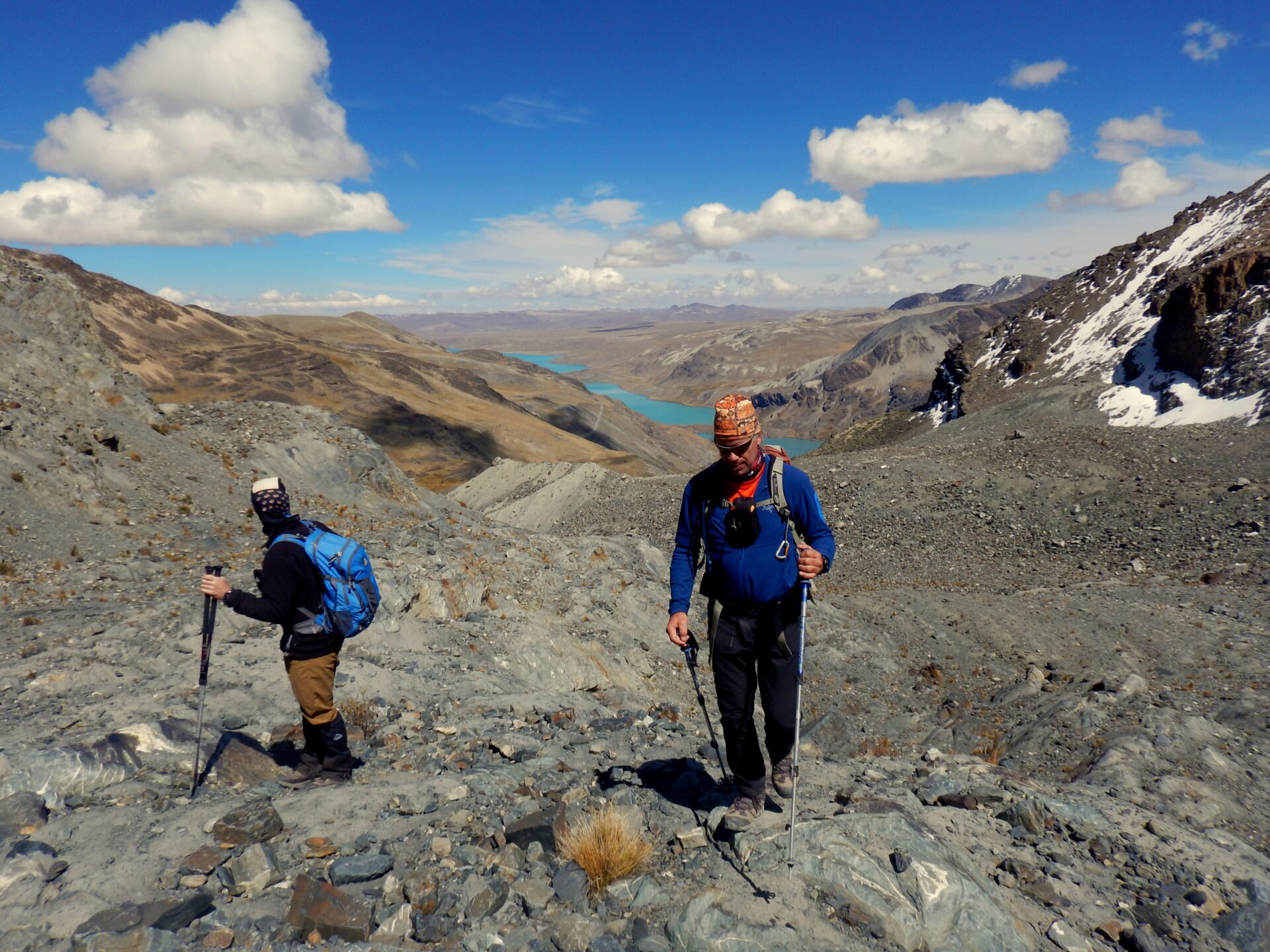 Deux randonneurs progressant sur un sentier rocailleux en haute altitude dans la Cordillère Royale, avec en arrière-plan un lac turquoise s’étendant entre les montagnes.