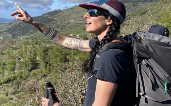 Anie Côté équipée, bâtons en main, pointant l’horizon avec enthousiasme sous un ciel dégagé.