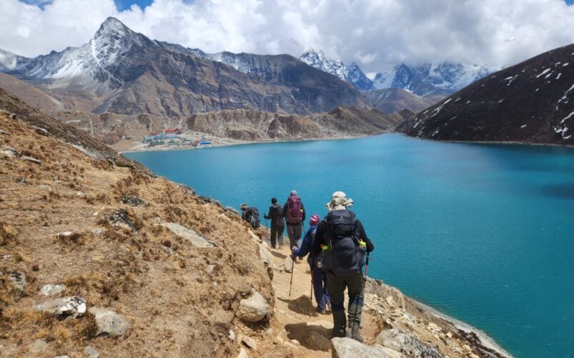 Randonnée sur les hauteurs du Népal, groupe de trekkeurs longeant un lac turquoise entouré de montagnes enneigées de l’Himalaya.