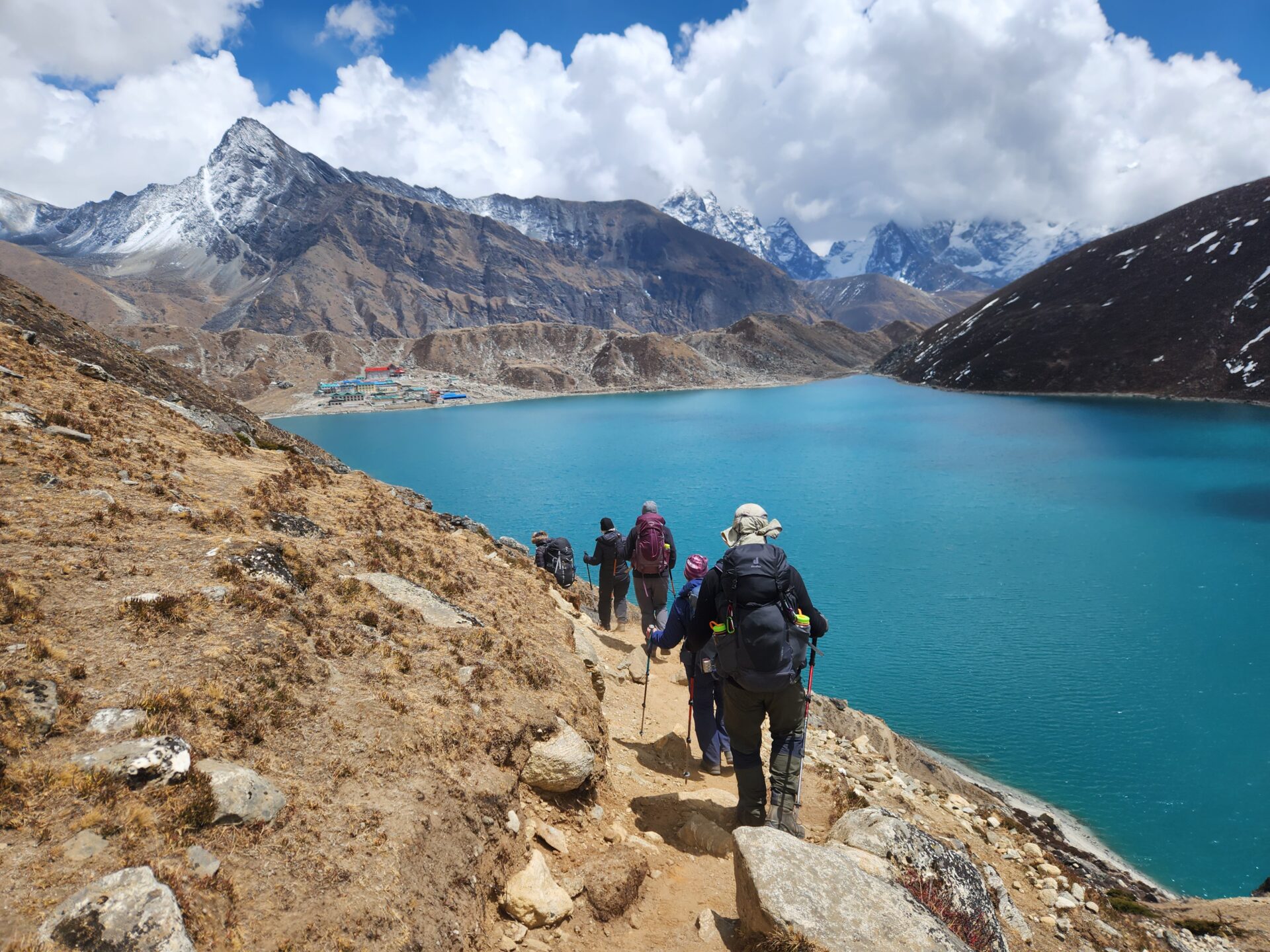 Randonnée sur les hauteurs du Népal, groupe de trekkeurs longeant un lac turquoise entouré de montagnes enneigées de l’Himalaya.