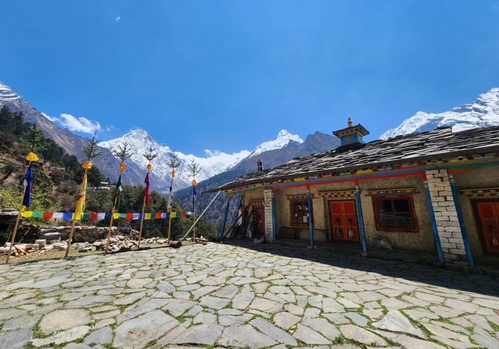 Cour d’un monastère bouddhiste dans la vallée de Tsum, drapeaux de prières flottant sous le ciel bleu