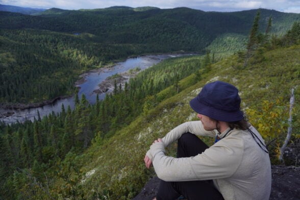Personne assise au bord d’une rivière en forêt.