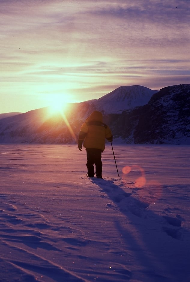 Silhouette d’un marcheur solitaire en parka avançant dans une vaste étendue enneigée, au coucher du soleil