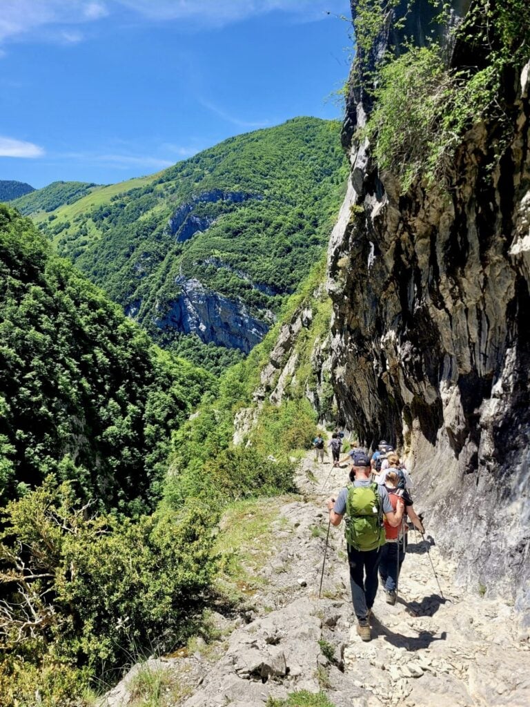 Randonneuse progressant dans un sentier étroit taillé dans la roche, montagnes verdoyantes en arrière-plan